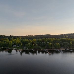 Puiden ja kivien ympäröimä Siilinlahden ranta Siilinjärvellä. Auringonlasku taustalla.