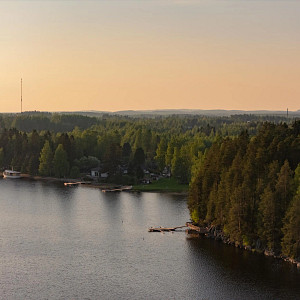 Puiden ja kivien ympäröimä Siilinlahden ranta Siilinjärvellä. Auringonlasku taustalla.