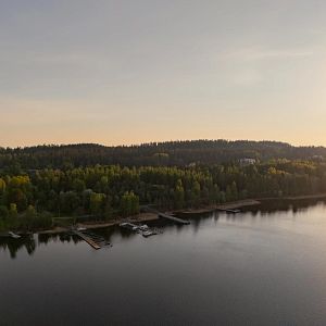 Puiden ja kivien ympäröimä Siilinlahden ranta Siilinjärvellä. Auringonlasku taustalla.