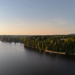 Puiden ja kivien ympäröimä Siilinlahden ranta Siilinjärvellä. Auringonlasku taustalla.