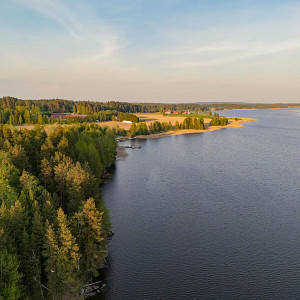 Puiden ja kivien ympäröimä Siilinlahden ranta Siilinjärvellä. Auringonlasku taustalla.