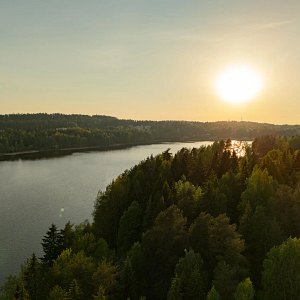 Puiden ja kivien ympäröimä Siilinlahden ranta Siilinjärvellä. Auringonlasku taustalla.