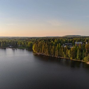 Puiden ja kivien ympäröimä Siilinlahden ranta Siilinjärvellä. Auringonlasku taustalla.
