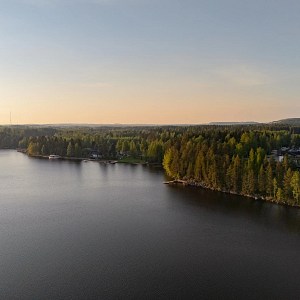 Puiden ja kivien ympäröimä Siilinlahden ranta Siilinjärvellä. Auringonlasku taustalla.